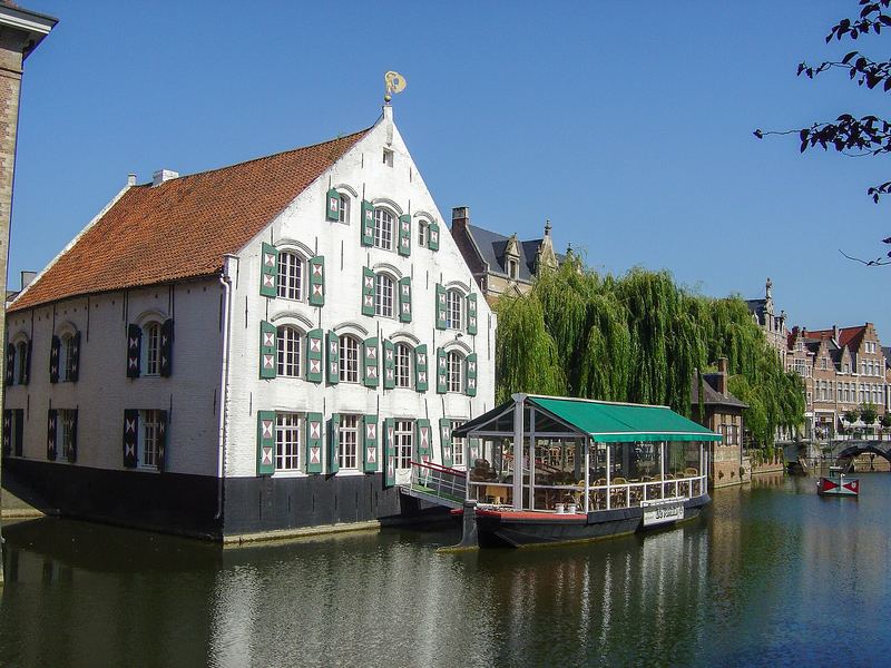 Een wit trapgevelhuis met groene luiken aan het water in Lier, met een rondvaartboot ervoor.